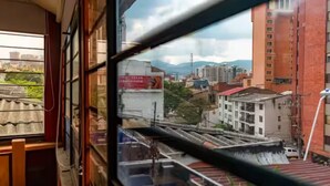 A view through a window with a metal frame, a metal railing, and a partial view of a building with a red brick facade. - SanAntonio Apartment in Cali, near the best attractions (Cali)