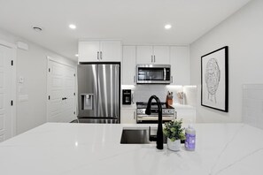 A modern kitchen with white cabinetry, stainless steel appliances, and a marble countertop. - New Modern 1Br Condo Near Airport (Calgary)