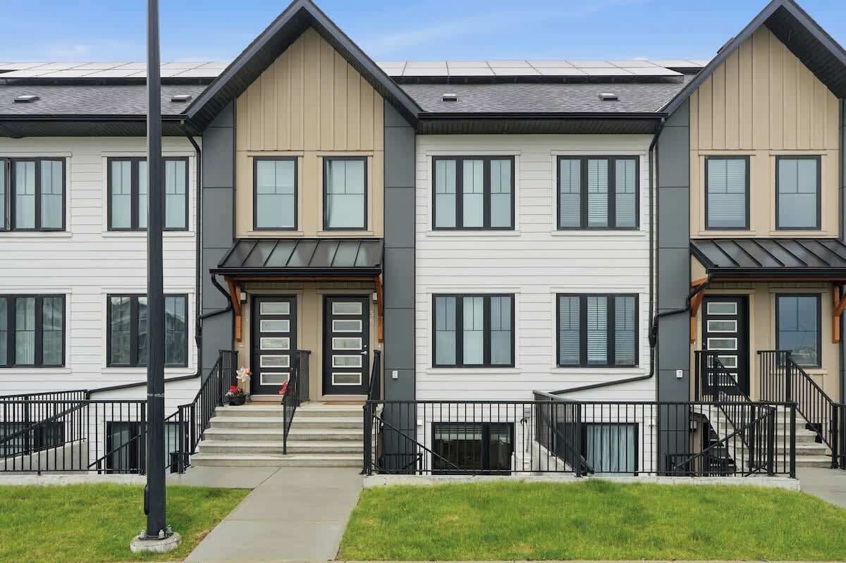 Une rangée de maisons de ville modernes à deux étages, caractérisées par une façade uniforme, de grandes fenêtres et une entrée centrale avec des marches.