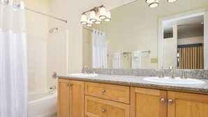 Un baño con bañera, dos lavamanos, armarios de madera y un espejo grande.