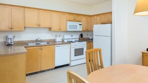 Una cocina con armarios de madera, microondas, estufa, refrigerador, lavaplatos y una mesa de comedor con sillas.