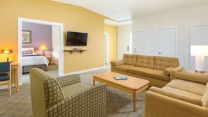 Una habitación de hotel con sofá, sillón y televisor montado en la pared.