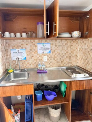 A compact kitchen with a sink, stove, and storage cabinets. There are signs on the wall and a variety of kitchenware on the shelves.