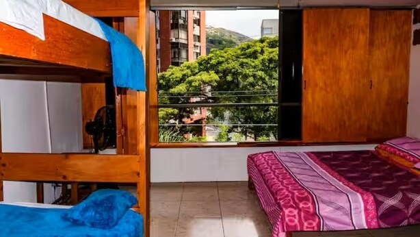 Ein Zimmer mit Etagenbetten, einem Fenster mit Blick auf Grünflächen und Gebäude sowie einem Kleiderschrank.