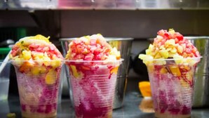 Drei Plastikbecher mit geschichteten Früchten und einer rosa Flüssigkeit, vermutlich ein Getränk, auf einer Metalloberfläche.