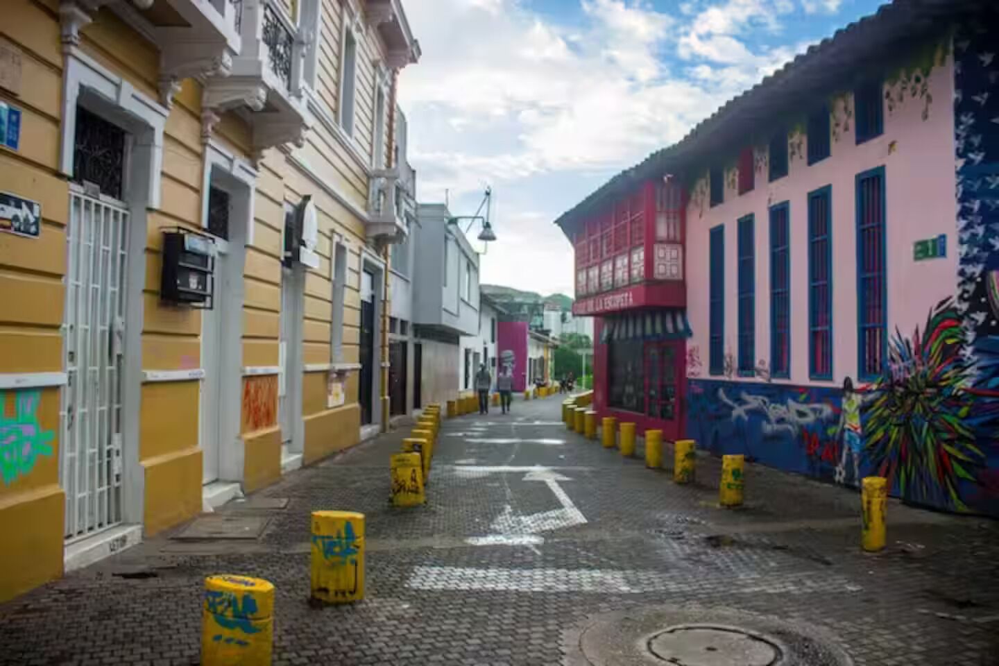 A narrow cobblestone street lined with colorful buildings, some with graffiti.