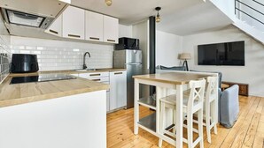 A modern kitchen with white cabinets, a stainless steel refrigerator, a wooden dining table, and a staircase. - Bastille · 12th · Apartment with Mezzanine – managed by Mey Agency (Paris)
