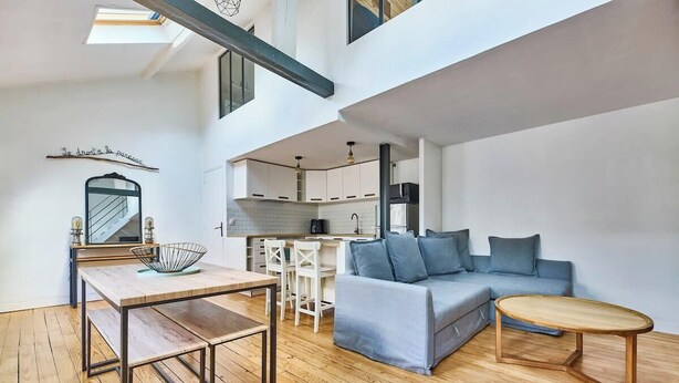 A modern loft apartment with a dining area, a sofa, and a kitchen in the background. - Bastille · 12th · Apartment with Mezzanine – managed by Mey Agency (Paris)