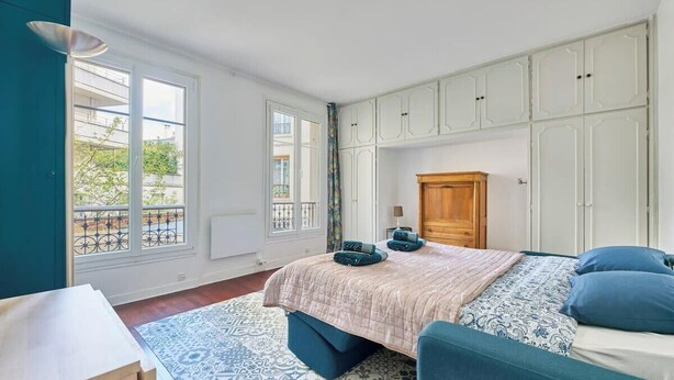 A bedroom with a bed, a wooden wardrobe, and a window with a view. - Convention · 15th · Colorful & Bright Studio – managed by Mey Agency (Paris)