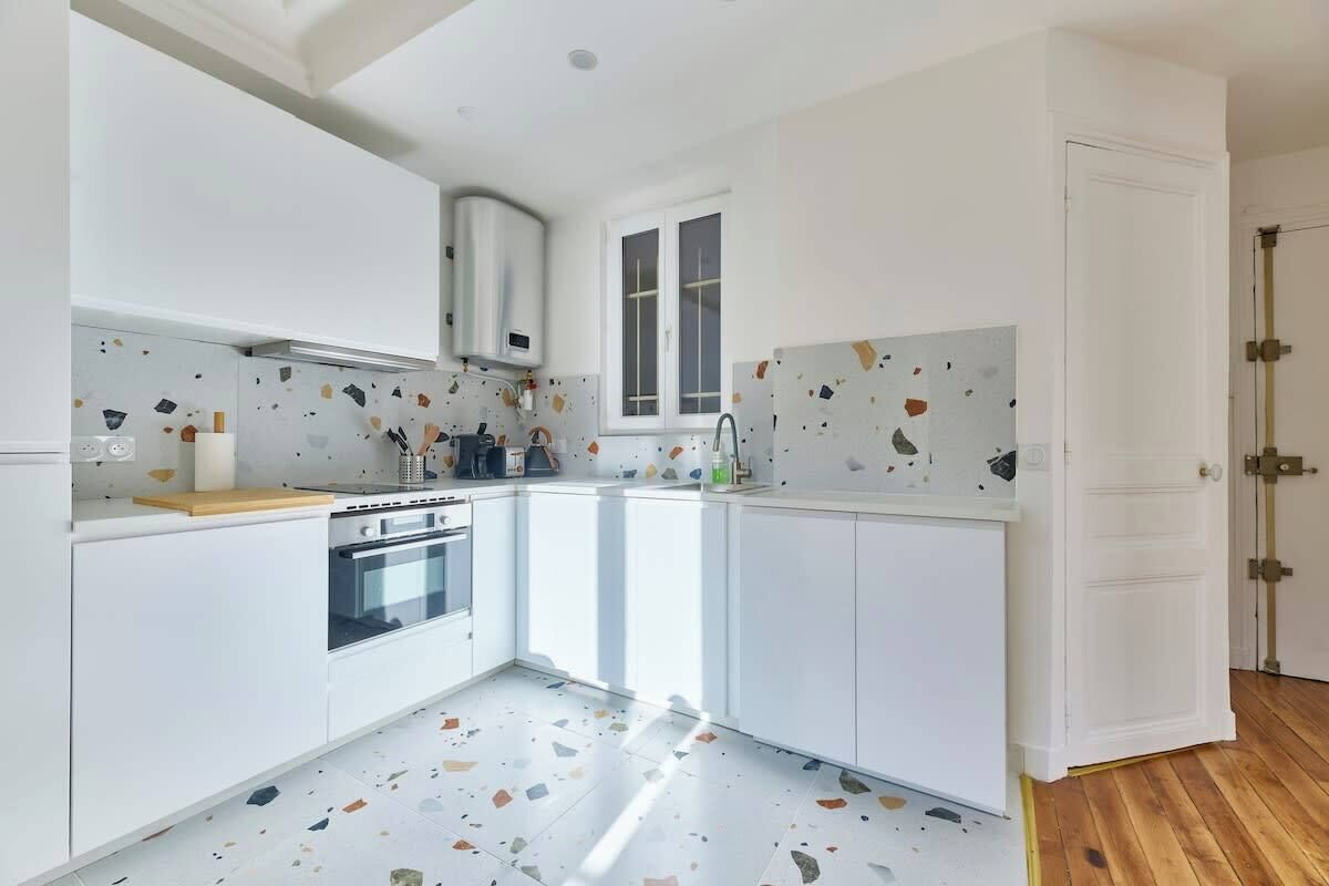 Une cuisine moderne avec des meubles blancs, un four encastré et une fenêtre.