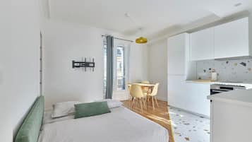 A modern bedroom with a bed, a small table, and a kitchenette.