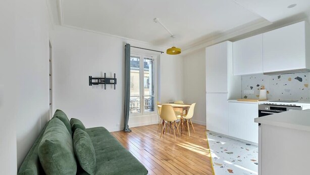 Una cocina moderna con armarios blancos, un comedor con mesa y sillas, y un sofá verde.