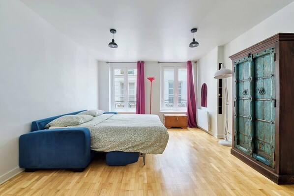 Une chambre à coucher avec un lit, un canapé bleu, une armoire et une fenêtre avec des rideaux.