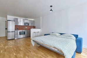 Ein Schlafzimmer mit einem Bett, einem blauen Kopfteil und einer Küchenzeile inklusive Kühlschrank, Backofen und Mikrowelle.