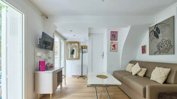 Una sala de estar moderna con un sofá, una mesa de centro, un televisor sobre un mueble bajo y obras de arte en las paredes.