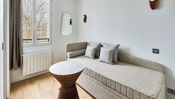 Ein modernes Wohnzimmer mit Sofa, rundem Couchtisch, einem Fenster mit Vorhängen, einer Heizung und Wanddekoration.