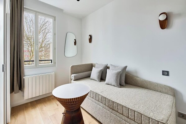 Ein modernes Wohnzimmer mit Sofa, rundem Couchtisch, einem Fenster mit Vorhängen, einer Heizung und Wanddekoration.