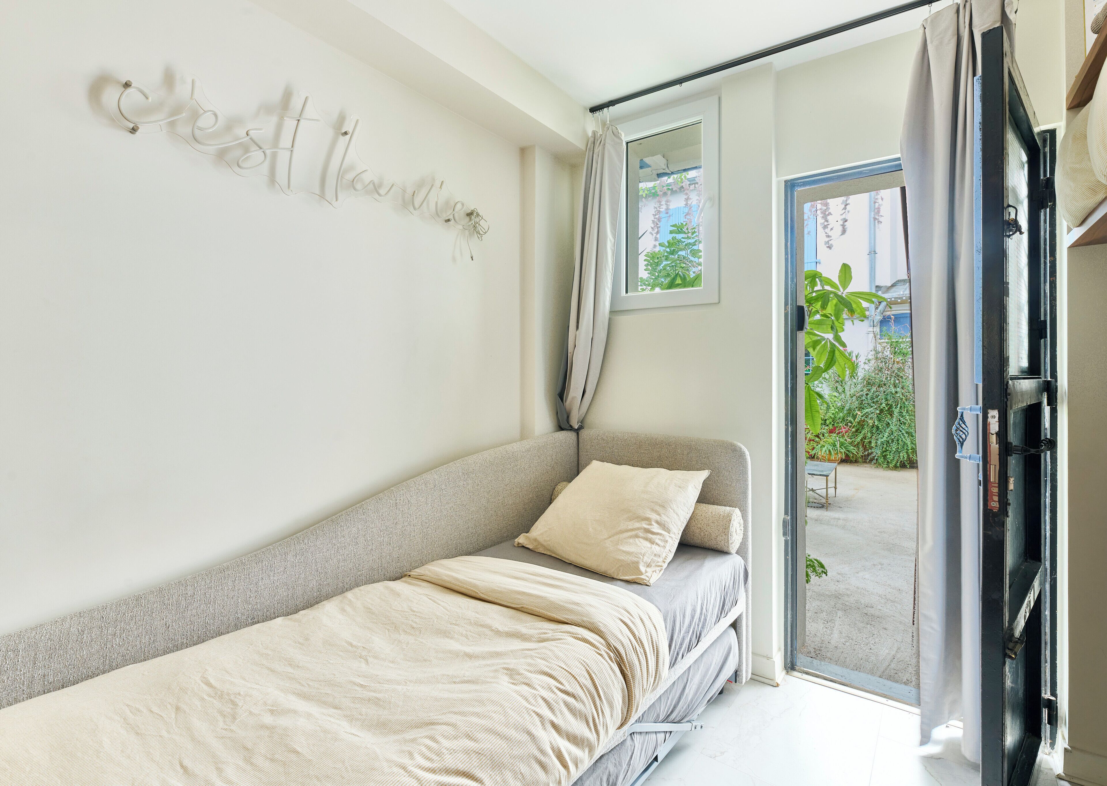 Ein schlicht eingerichtetes Schlafzimmer mit einem Bett, einem Fenster mit Vorhängen und einem Wandbild.