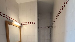 Ein Badezimmer mit weißen Fliesen, einem spiegelnden Holzrahmen, einem Waschbecken, einer Toilette und einer Dusche.