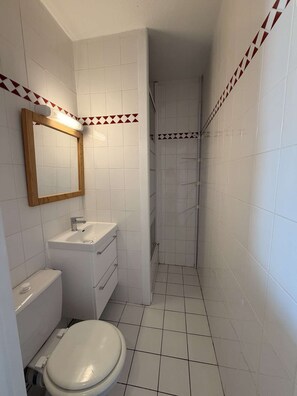 A bathroom with white tiles, a wooden-framed mirror, a sink, a toilet, and a shower. - Seignosse Océan, one-bedroom apartment near the beach, quiet, pine forest, family of 4 (SEIGNOSSE)