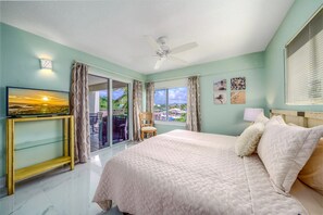 Une chambre à coucher avec un lit, un téléviseur posé sur un meuble, un ventilateur de plafond et une vue par la fenêtre.