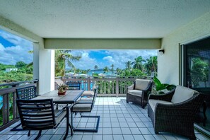 Un balcon agrémenté d’une table, de chaises et d’un canapé, offrant une vue sur un paysage tropical avec des palmiers et une piscine.