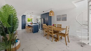 Una cocina moderna con armarios oscuros, una isla central y un comedor con sillas y una mesa de madera.