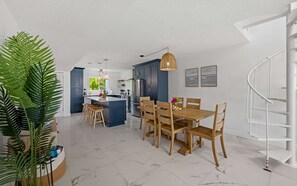 Eine moderne Küche mit dunklen Schränken, einer zentralen Kochinsel und einem Essbereich mit Holztischen und -stühlen.