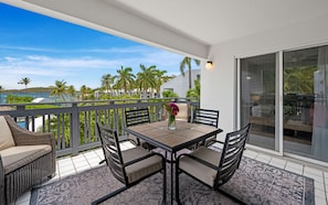 Ein Balkon mit Tisch und Stühlen, eine Vase mit Blumen und Blick auf Palmen und einen Strand.
