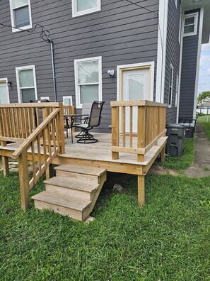 A wooden deck with a chair and a table, a small set of stairs leading to a door, and a trash bin. - Modern Indianapolis Retreat 3BR/2.5BA Minutes to Hospitals & Downtown (Indianapolis)