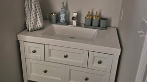 Un baño con un tocador blanco, un espejo redondo y un perchero para toallas.