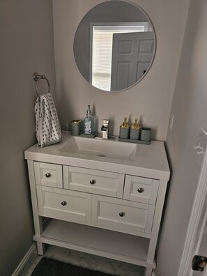 A bathroom with a white vanity, a round mirror, and a towel rack.