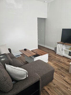 A modern living room with a sectional sofa, a wooden coffee table, and a white entertainment unit. - Modern Indianapolis Retreat 3BR/2.5BA Minutes to Hospitals & Downtown (Indianapolis)