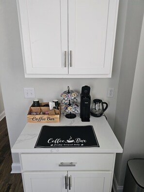 Una encimera de cocina con un espacio para café, que incluye una cafetera, un molinillo de café y una taza.