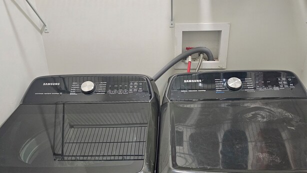 Dos lavadoras Samsung negras una al lado de la otra, con una pared blanca y un estante encima.
