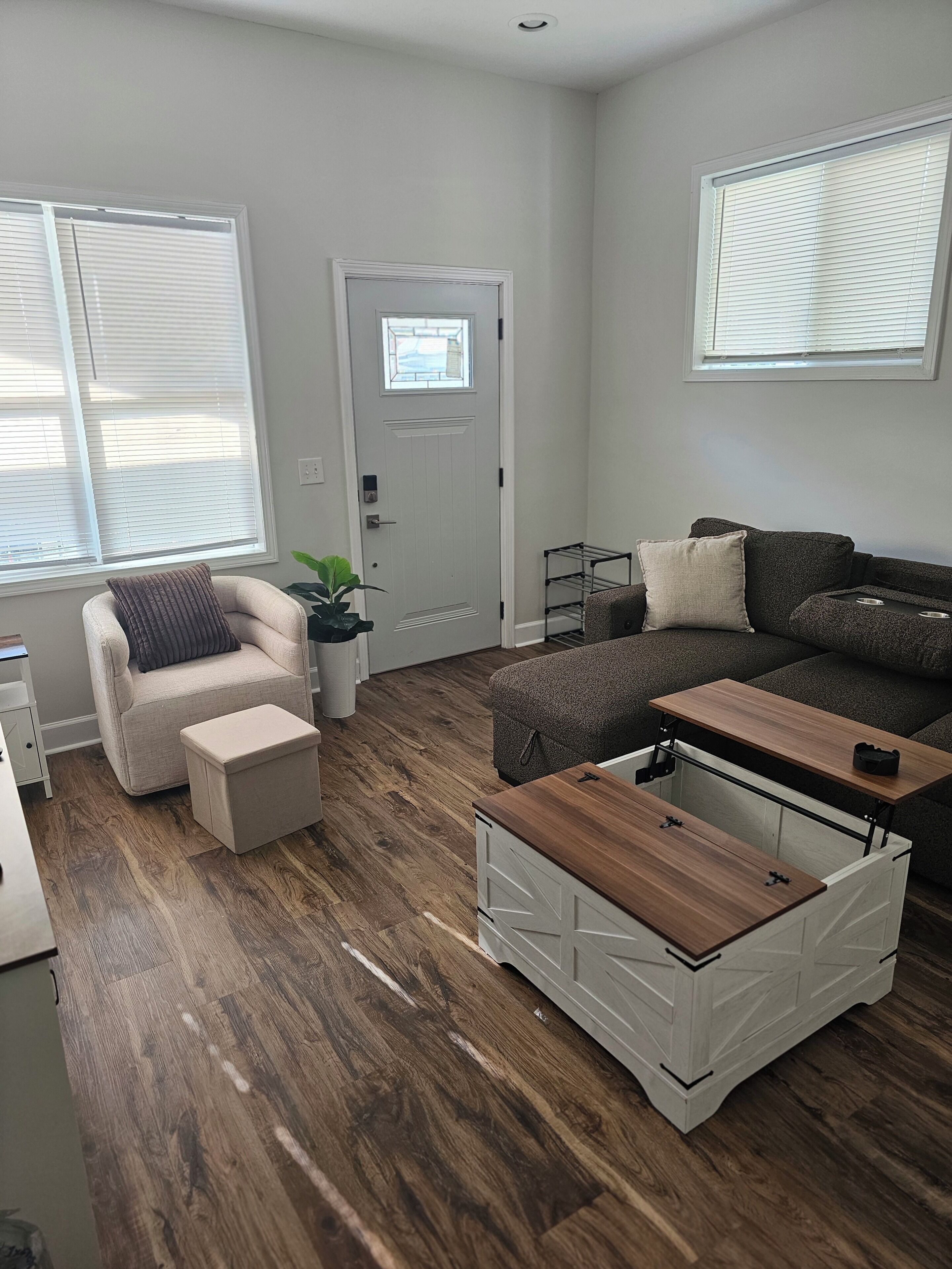 Un salon moderne comprenant un canapé, un fauteuil, un pouf et une table basse en bois.