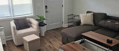 A modern living room with a sofa, armchair, ottoman, and a wooden coffee table.