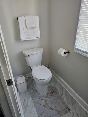 A bathroom with a toilet, a towel rack, a toilet paper holder, and a marble floor.