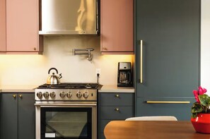 A kitchen with a gas stove, oven, coffee maker, and a potted plant.