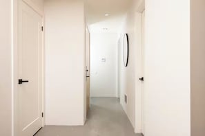 A narrow hallway with white walls, a ceiling light, and a door on the left.