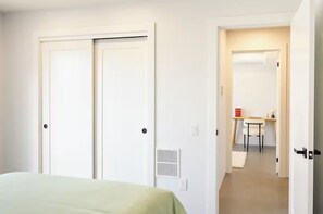 A bedroom with a bed, a desk, and a chair in a hallway.