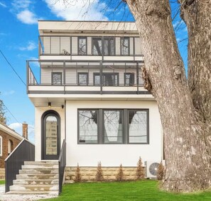 A modern two-story house with a balcony, large windows, and a stone foundation.