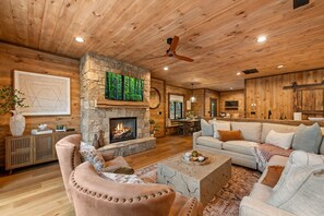 A cozy living room with a stone fireplace, wooden ceiling, and a large sofa. - Enjoy a Cozy Couples Retreat: Serene • Hot-Tub • Fire-Pit • Close to Dtwn + Lake (Blue Ridge)