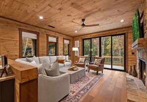 A spacious living room with a wooden ceiling, a sofa set, a coffee table, and a fireplace. - Cottage at Fern Cove: Couples • Serene • Hot-Tub • Fire-Pit • Close to Downtown (Blue Ridge)