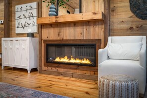 A living room with a fireplace, wooden paneling, a white sofa, and a cabinet. - Cottage at Fern Cove: Couples • Serene • Hot-Tub • Fire-Pit • Close to Downtown (Blue Ridge)