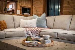 A cozy living room with a beige sofa, a wooden coffee table with a tray of items, and a wooden wall. - Cottage at Fern Cove: Couples • Serene • Hot-Tub • Fire-Pit • Close to Downtown (Blue Ridge)
