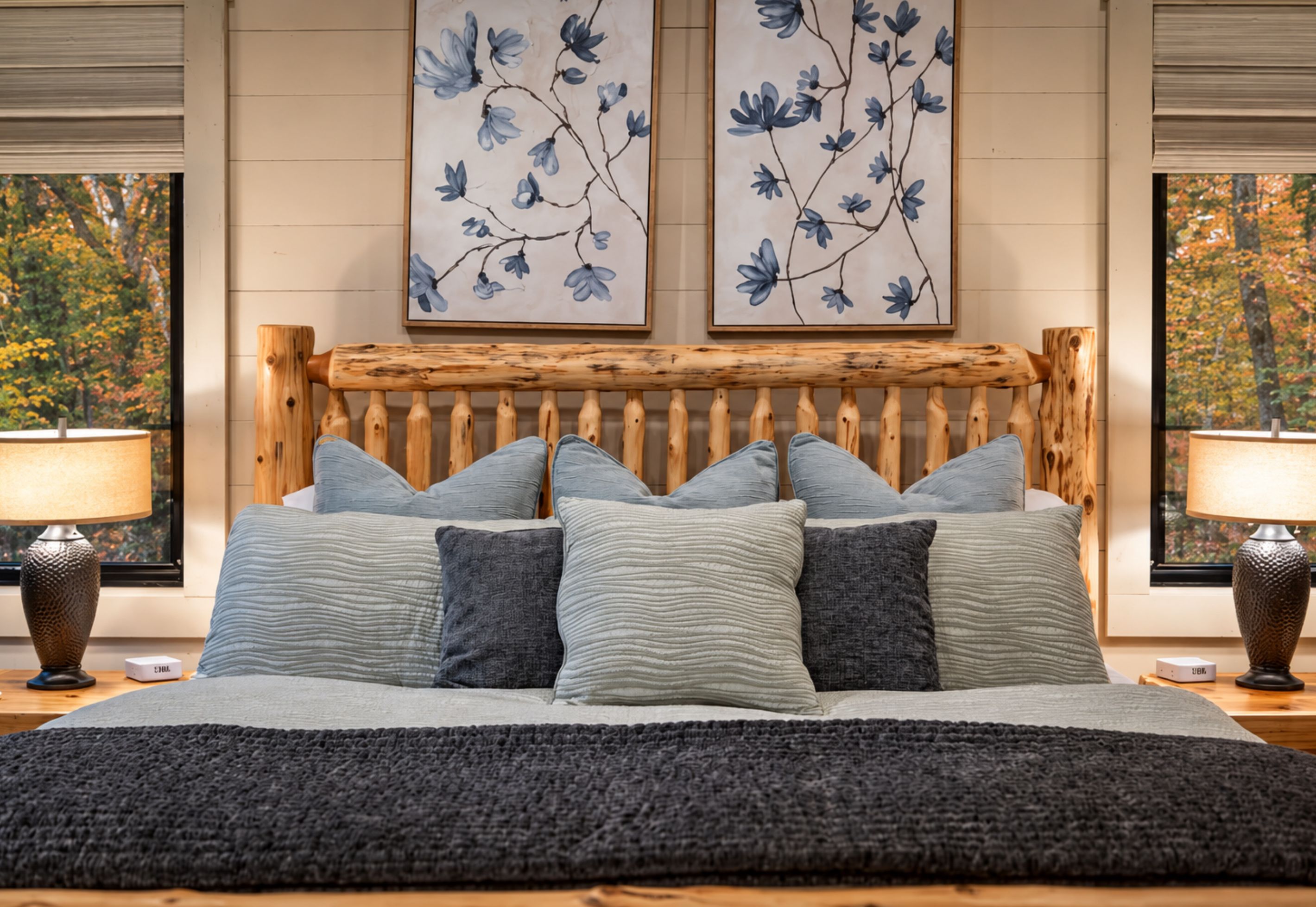 Een slaapkamer met een houten hoofdeinde, meerdere kussens en twee bloemende schilderijen aan de muur.