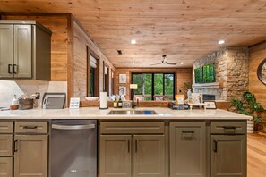 A kitchen with wooden cabinets, a stone accent wall, a large window, and a built-in oven. - Enjoy a Cozy Couples Retreat: Serene • Hot-Tub • Fire-Pit • Close to Dtwn + Lake (Blue Ridge)