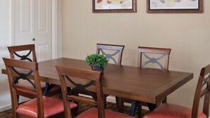 Une table à manger avec six chaises, une plante en pot et deux tableaux encadrés accrochés au mur.