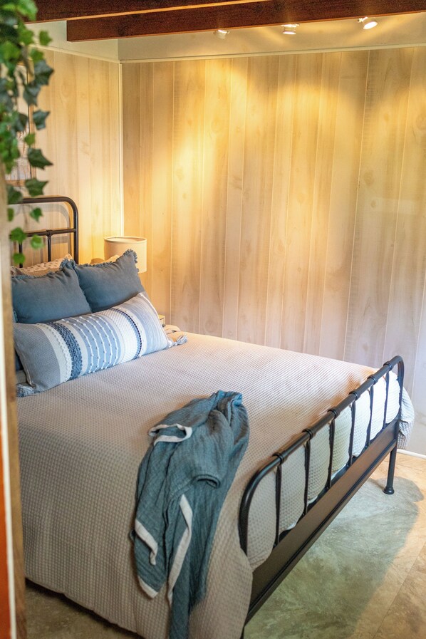 Ein Schlafzimmer mit einem Bett, Kissen, einer Lampe und einer hängenden Pflanze.